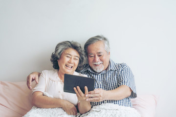 Senior couple using a tablet phone computer face time call to relatives descendant relatives grandchild, smiling feel happy in sofa at home - lifestyle senior concept