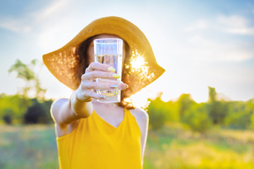 Happy beauty young woman female with pure glass of water wears yellow lite dress and summer hat...