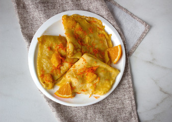Traditional French crepes Suzette with orange sauce on white plate over marble background