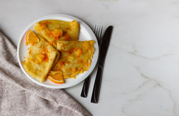 Traditional French crepes Suzette with orange sauce on white plate over marble background. Сopyspace for your text