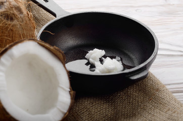 Coconut, shell with meat, cast iron skillet on hemp sackcloth on white wooden kitchen table