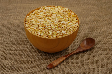 Raw yellow plate with wooden spoon and spoon against the background of burlap texture