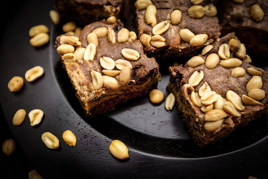 Homemade brownies with peanuts on a dark brown plade