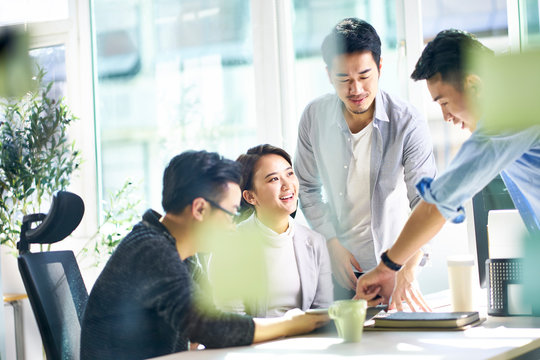 group of four asian teammates working together discussing business in office