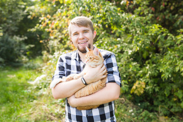 Naklejka na ściany i meble people, summer tourism and animals concept - handsome young man with cute cat outdoors