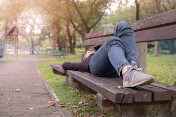 A woman is sleeping on the bench in the park.