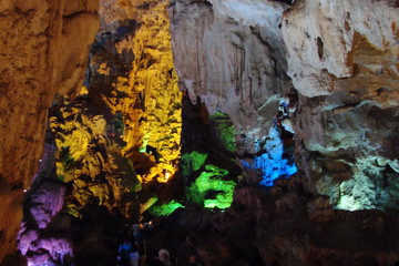 The unique landscape of stalactites and stalagmites of various shapes and sizes in the rocky caves of small islands under the rays of colorful illumination.