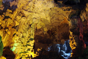 The unique landscape of stalactites and stalagmites of various shapes and sizes in the rocky caves of small islands under the rays of colorful illumination.