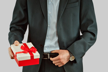 A man in a suit holds a gift box in his hands. Box with a red ribbon and a bow.