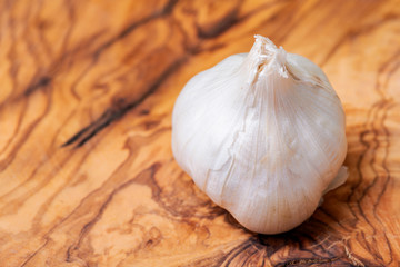 Organic Raw Whole Garlic bulb placed on natural olive wood. Allium sativum.