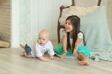 girl in a white shirt and blue skirt playing with baby brother in a white shirt and jeans sitting next to the fireplace on the floor. A family