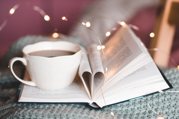 Cup of tea on open book with heart shape over glowing lights closeup. Good morning. Love concept.