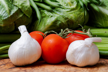 Organic Raw Whole Garlic bulbs and  Red Tomatoes on the vine arranged on natural olive wood. Allium sativum. Solanum lycopersicum.