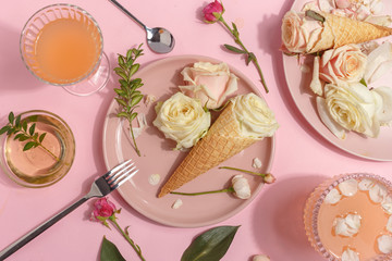 Light pink set of dishes on the table. Delicate rosebuds of pastel colors and petals on a plate and waffle cones. Top view.