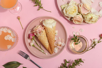 Light pink set of dishes on the table. Delicate rosebuds of pastel colors and petals on a plate and waffle cones. Top view.