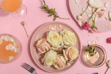 Light pink set of dishes on the table. Delicate rosebuds of pastel colors and petals on a plate and waffle cones. Top view.