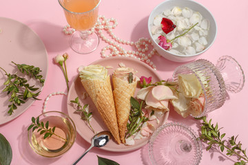 Light pink set of dishes on the table. Delicate rosebuds of pastel colors and petals on a plate and waffle cones. Top view.