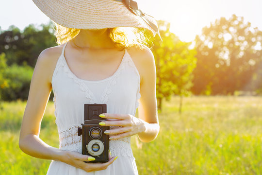 Happy beautiful fun girl woman hipster wear straw hat long white dress hold take picture old ancient rare photo camera on big large wide summer hot spring sunny green light field between fruit trees