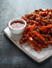 Crispy shredded beef with carrots and sweet chilli sauce on white wooden board. Chinese takeaway food