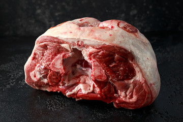 Raw lamb leg on black stone table.