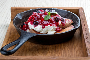 Breakfast in a pan on a white background. Pancakes with cream and jam. On a wooden tray.