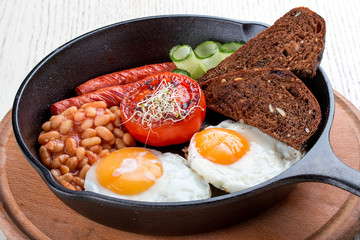 Breakfast in a pan on a white background. Scrambled eggs with beans, toast and sausages.