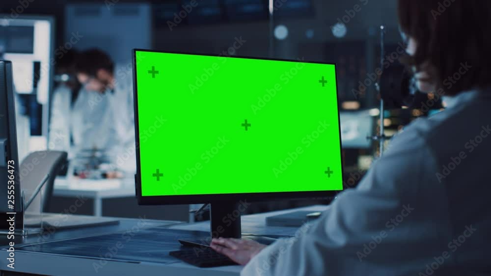Wall mural over the shoulder shot: female it scientist uses green mock-up screen computer. in the background te