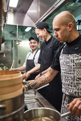 Positive atmosphere. Vertical photo of chef and his smiling assistants preparing food together in a kitchen.