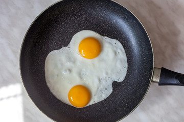 Fried eggs cooked in frying pan for breakfast, top view