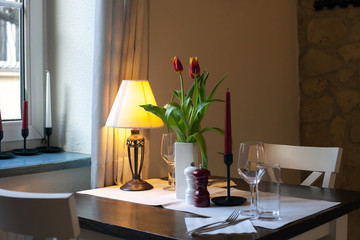 Dining wooden table with white tablecloth, tulips bouquet and glasses