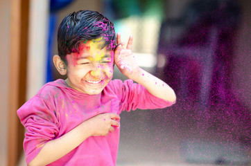Cute Little Indian boy child with coloured face paint poweder color thrown at his face during holi indian festival looking at camera
