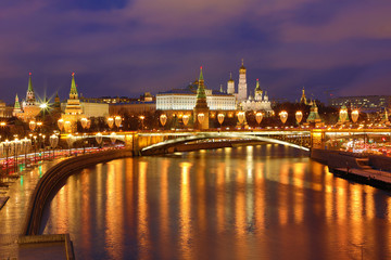 Fototapeta premium Illuminated Moscow Kremlin and Bolshoy Kamenny Bridge in the rays of setting sun. View from the Patriarshy pedestrian Bridge in Russia. Evening urban landscape in the blue hour