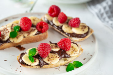 Light summer breakfast or lunch with sandwiches of white bread with chocolate paste, bananas and raspberries on the background of the village table