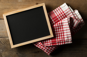 Blank, empty, black chalkboard with red checkered dish towel flat lay from above on brown wooden table