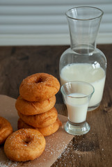 Top view of donuts in stack with bottle of milk and glass of milk on wooden background and white wall