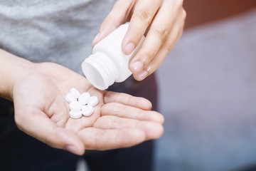 close up man hand holding a medicine, with pours the pills out of the bottle. Caring for the health 