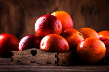 Juicy ripe shiny red bloody oranges in tray for making refreshing cocktail on rustic wooden table background, still life, selective focus