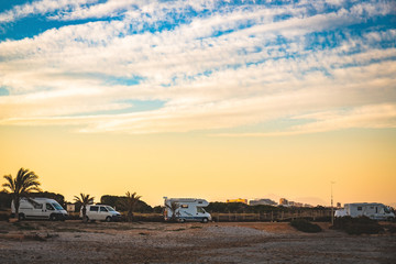 Motorhome making wild camp on the beach at a beautiful sunset or sunrise with mountains in the background. Caravan parked on the beach in front of the blue sea in a beautiful place of wild nature