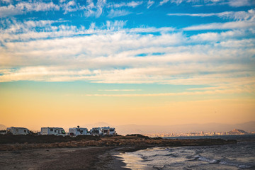 Obraz premium Motorhome making wild camp on the beach at a beautiful sunset or sunrise with mountains in the background. Caravan parked on the beach in front of the blue sea in a beautiful place of wild nature