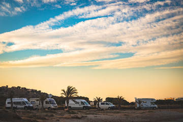 Motorhome making wild camp on the beach at a beautiful sunset or sunrise with mountains in the background. Caravan parked on the beach in front of the blue sea in a beautiful place of wild nature