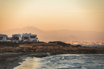 Motorhome making wild camp on the beach at a beautiful sunset or sunrise with mountains in the background. Caravan parked on the beach in front of the blue sea in a beautiful place of wild nature