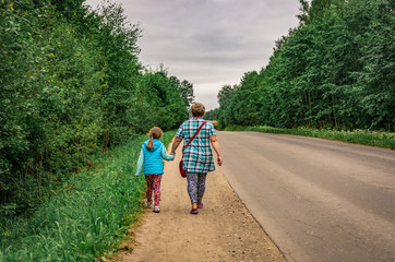 Mom and little daughter go by the hand along the road in the countryside