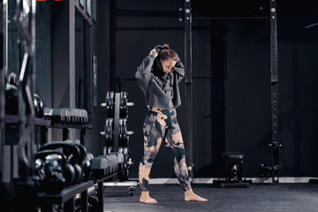 Fototapeta na wymiar Young Caucasian female bodybuilder putting hoodie on while standing in gym at night.