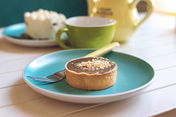 Salted caramel round cake on blue plate with fork, yellow tea pot and green cup. Delicious caramel chocolate tart, topped with nuts