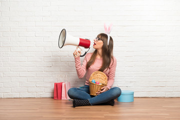 Woman with bunny ears for Easter holidays sitting on the floor shouting through a megaphone to...