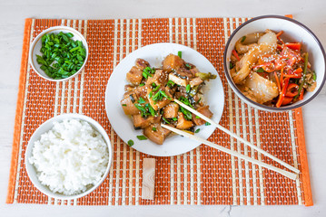Traditional Asian lunch - spicy pork, rice, salad with Chinese cabbage, peppers and tomatoes. Korean dinner with pork belly, rice, kimchi salad