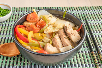 Suan cai - traditional Chinese stew of pork and pickled Chinese cabbage in a black bowl on a bamboo napkin.