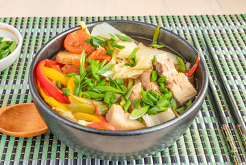 Suan cai - traditional Chinese stew of pork and pickled Chinese cabbage in a black bowl on a bamboo napkin.