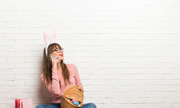 Woman with bunny ears for Easter holidays sitting on the floor keeping a conversation with the mobile phone with someone