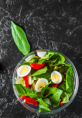 spinach salad with eggs, pepper and tomatoes in glass bowl on dark background